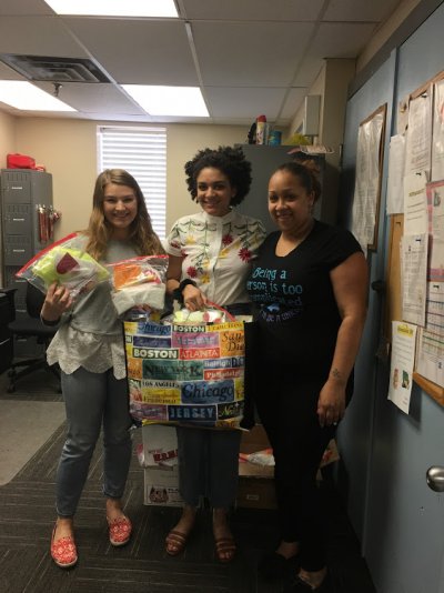 three young women standing together showcasing donated items for feminine hygiene 