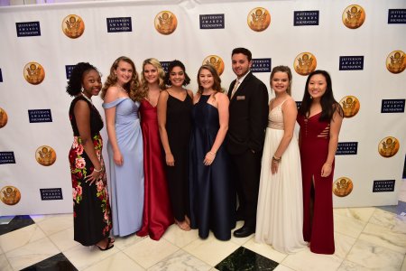 Diverse group of students dressed in formal attire standing in front of a Jefferson Award banner